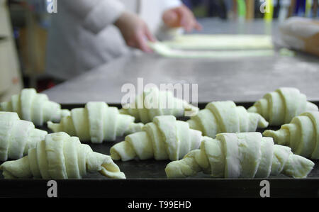 Materie croissant disposti su una placca da forno. Preparazione della cottura di pasta in una pasticceria. Professional baker occupazione. Foto Stock