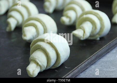 Materie croissant disposti su una placca da forno. Preparazione della cottura di pasta in una pasticceria. Foto Stock