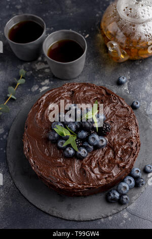 Torta al cioccolato con teiera e tazze su sfondo scuro. Vista laterale, il concetto di vacanza per celebrare il cibo Foto Stock