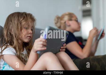 Le ragazze sono sedute sul divano e la lettura. La donna trattiene compressa mentre la ragazza ha il telefono in mano Foto Stock
