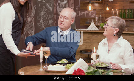 Uomo senior di pagare il conto con la sua carta di credito in un ristorante. Coppia senior presso il ristorante. Romantico vecchia coppia. Foto Stock
