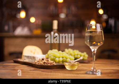 Ciotola di squisito miele dorato accanto a un bicchiere di vino bianco. Formaggio francese. Uve fresche. Foto Stock