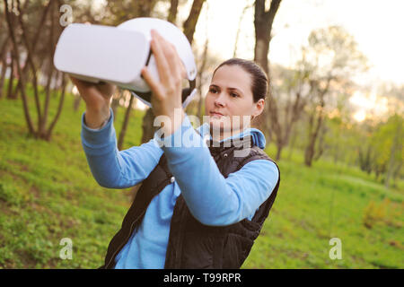 La ragazza con gli occhiali di realtà virtuale sullo sfondo del verde e del Parco Foto Stock