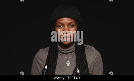Ritratto di donna africana in tshirt avente lunghi dreadlocks. Ritratto di donna africana isolato su sfondo nero. Foto Stock