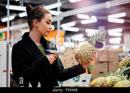 Giovane donna attraente holding scanner di codici a barre e la scansione dei prodotti in negozio. Concetto moderno di gadget e periferiche, la frutta e la verdura departmen Foto Stock