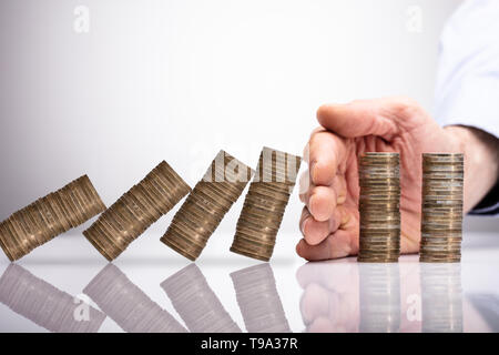 Close-up di un imprenditore la mano proteggere le monete impilate di cadere sulla scrivania riflettente Foto Stock