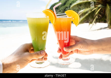 Close-up del giovane la mano tostare i bicchieri di cocktail presso la spiaggia durante la stagione estiva Foto Stock