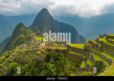 Alcuni turisti che si godono la vista dalle terrazze di agricoltura su perso rovine Inca di Machu Picchu, Cusco, Perù. Foto Stock