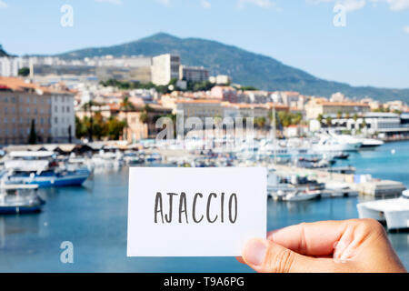 Primo piano della mano di un giovane uomo caucasico tenendo un cartello bianco con la parola Ajaccio scritto in esso, al porto di Ajaccio in Corsica, Francia Foto Stock