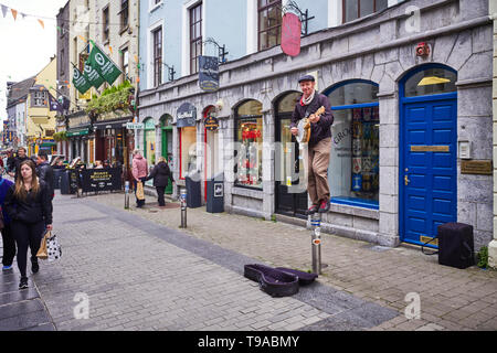 Un banjo suonatore ambulante riproduzione permanente sulla sommità di una piccola strada bollard nel centro di Galway Foto Stock