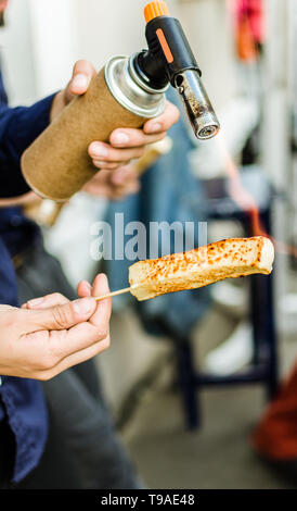 Un chef formaggio grill con un gas da cucina torcia presso un mercato alimentare Foto Stock