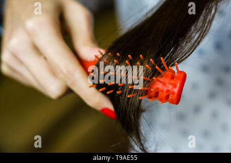 Bruna giovane donna pettinare i suoi capelli castani. Messa a fuoco selettiva. Foto Stock