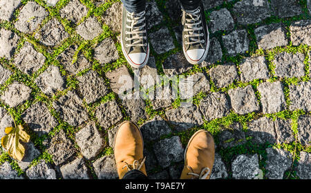 Piedi e gambe di una coppia felice in amore contro verde pavimentazione in pietra sullo sfondo Foto Stock