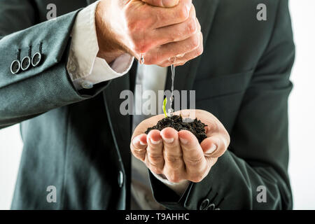 Primo piano di imprenditore irrigazione e coltivando un germoglio verde crescente a partire da un terreno fertile sta tenendo nella sua mano a tazza. Concettuale del business ad elevata visibilità Foto Stock