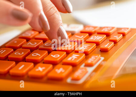 Vista dettagliata del ragioniere femmina premendo numero otto su orange calcolatrice da tavolo in una contabilità, ricerca o istruzione concetto. Foto Stock