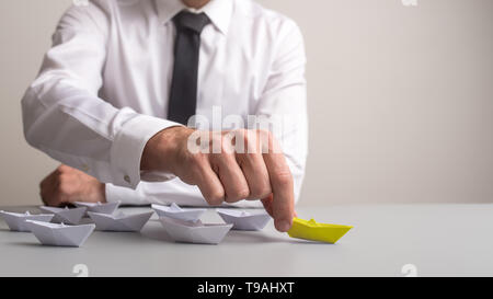 Business executive spingendo in avanti prima di molti fatti di carta origami barche che si distingue anche dal colore giallo. Foto Stock