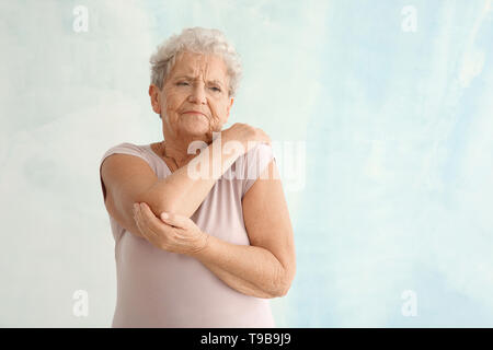 Senior donna che soffriva di dolori al gomito sul sfondo luminoso Foto Stock