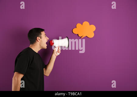 Urlando giovane con megafono vicino al discorso bolla sul colore di sfondo Foto Stock