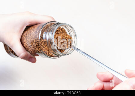 Mano spooning fino caffè istantaneo da un barattolo di vetro sopra il tavolo Foto Stock