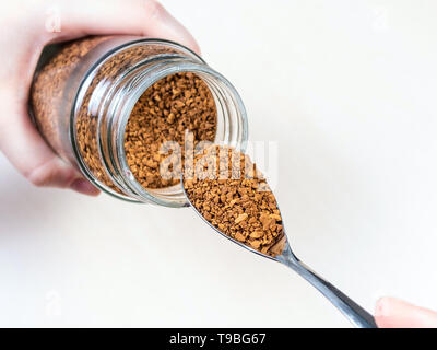 Spooning fino porzione di caffè istantaneo da un barattolo di vetro sopra il tavolo Foto Stock