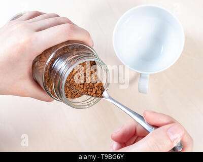 Vista superiore del cucchiaio nel vasetto di vetro con caffè istantaneo su cup in marrone chiaro tabella Foto Stock