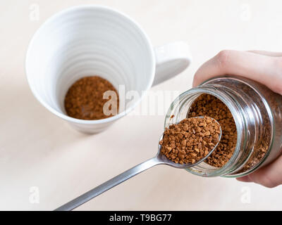 Cucchiaio vicino al vaso di vetro con caffè istantaneo su mug in marrone chiaro tabella Foto Stock