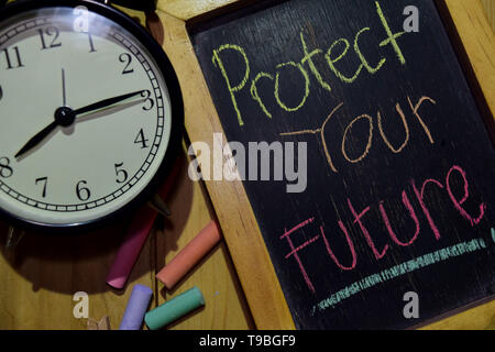 Proteggi il tuo futuro su una frase colorata manoscritta su lavagna e sveglia con motivazione, ispirazione e concetti di istruzione. Sfondo tabella Foto Stock