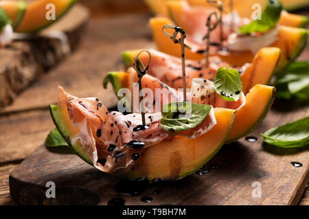 Fette di Melone con prosciutto e le foglie di basilico, servita su una tavola di legno tagliere close up Foto Stock