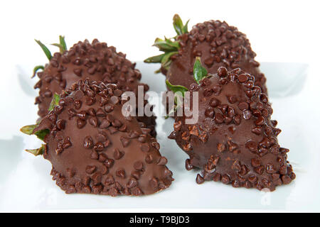 Chiudere fino a quattro succose fragole affogate nel cioccolato fondente spolverati con mini scaglie di cioccolato su una piastra isolata su bianco. Foto Stock