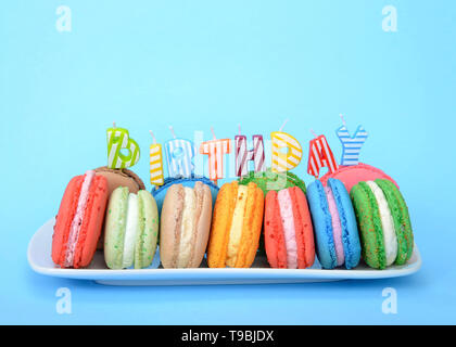 Molte colorate macaron i cookie su un bianco piastra rettangolare, candeline di compleanno l'ortografia della parola compleanno su sfondo blu con una copia dello spazio. Foto Stock