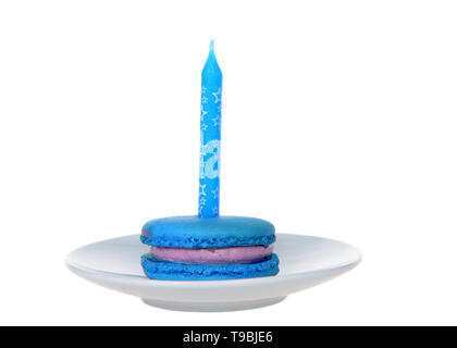 Blue macaron cookie con viola ripieno di panna su una piastra bianca con candela blu isolato su bianco. Festa di compleanno del tema. Foto Stock