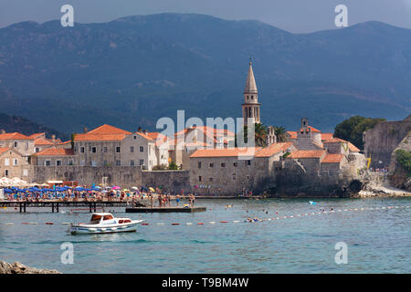 City beach e tetti in tegole rosse della città vecchia di Budva contro le montagne e il cielo. Montenegro. Agosto 2018. Foto Stock