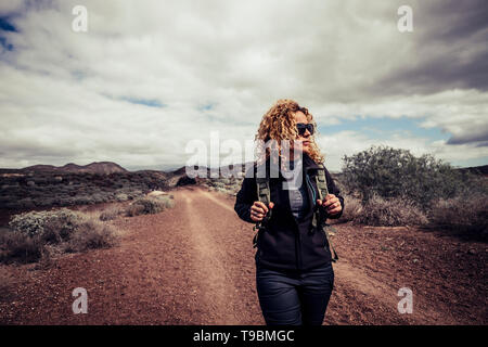 Bella trekker caucasica ricci biondo giovane donna attiva a piedi nel percorso del Deserto godere della libertà e di uno stile di vita attivo in viaggio con backp Foto Stock