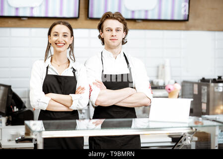 Ritratto di un uomo e di una donna in nero grembiuli in piedi insieme come venditori nella moderna pasticceria o cafe Foto Stock