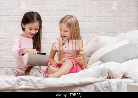 Due simpatici ragazzi ragazze utilizzare tavoletta digitale a letto. bambini che giocano su tablet pc. Foto Stock