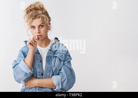 Perplesso turbato grave-cercando creative smart blonde curly-dai capelli donna bionda bite pollice sguardo rivolto a risolvere la situazione problematica, pensando di rendere Foto Stock