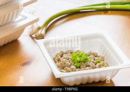 Natto - un popolare e sano cibo giapponese dalla fermentazione dei fagioli in un contenitore di polistirolo con verde cipolline come condimenti. Foto Stock