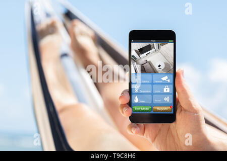 Close-up di una donna sdraiata sulla amaca tenendo il telefono cellulare con applicazioni su Smart Home Foto Stock