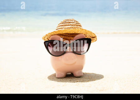 Rosa Piggybank indossando occhiali da sole neri sulla sabbia in spiaggia Foto Stock