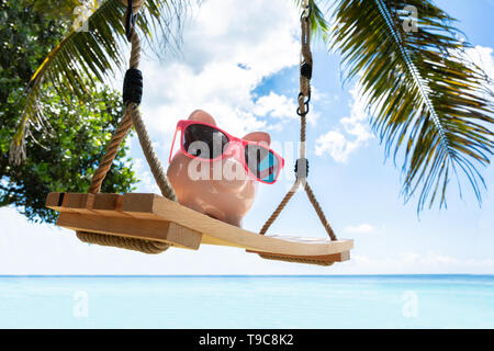 Close-up di Rosa Piggybank con gli occhiali da sole sul brandeggio in legno a Beach Foto Stock