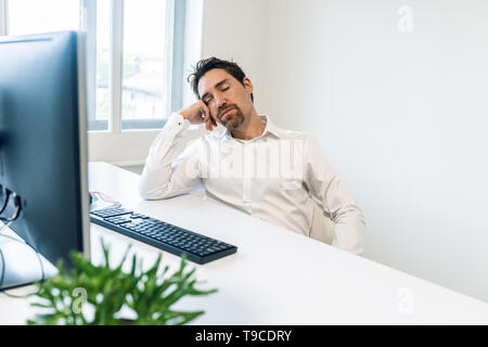 Oberati di lavoro giovane imprenditore a dormire la sua scrivania da ufficio poggiando sulla sua mano. Foto Stock
