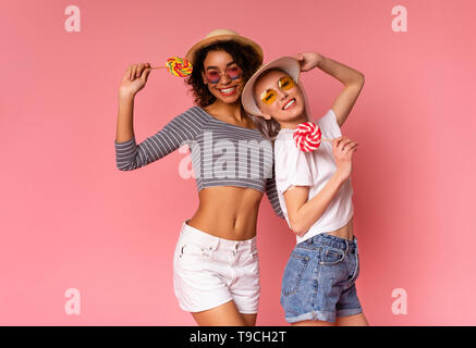 Positive le donne millenaria che posano con connettori lollipop su sfondo rosa Foto Stock