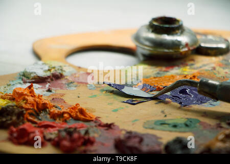 Primo piano della tavolozza con vernici colorate ed una spatola sulla superficie bianca, lo sfondo o il concetto Foto Stock