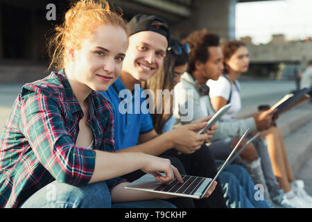 Carino redhead ragazza utilizzando laptop, studiando con i suoi amici teen Foto Stock