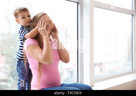 Giovane donna incinta giocando con il suo grazioso piccolo figlio vicino a finestra Foto Stock