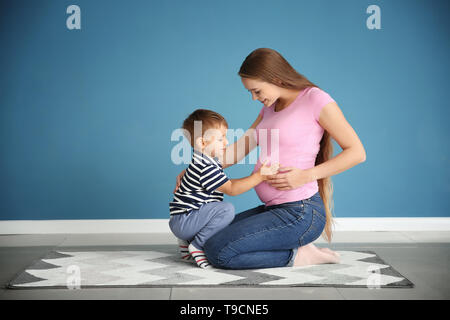 Carino piccolo ragazzo di toccare la pancia di sua madre gravida seduti su un tappeto Foto Stock