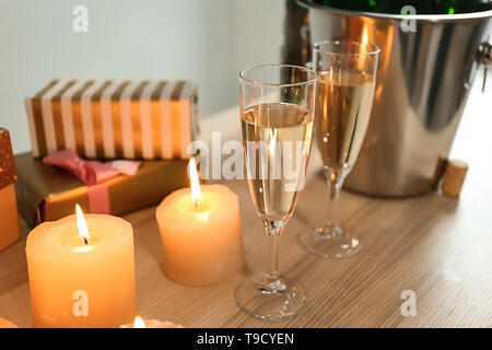 Bicchieri di champagne con candele accese e confezioni regalo sul tavolo di legno Foto Stock