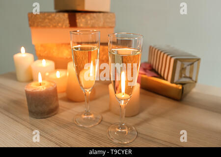 Bicchieri di champagne con candele accese e confezioni regalo sul tavolo di legno Foto Stock