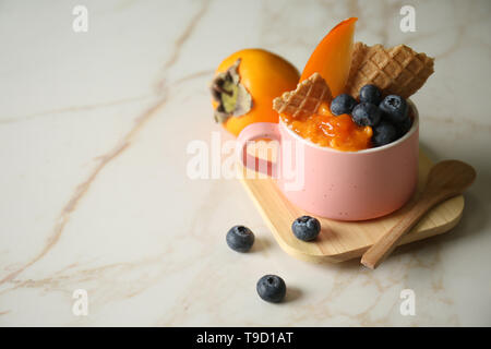 Gustosi dessert con maturi, persimmon waffle e mirtilli in coppa sul tavolo luminoso Foto Stock