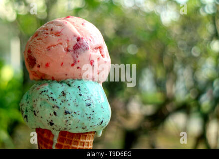 La fusione di due palline di gelato in cono di luce solare contro sfocate fogliame verde Foto Stock